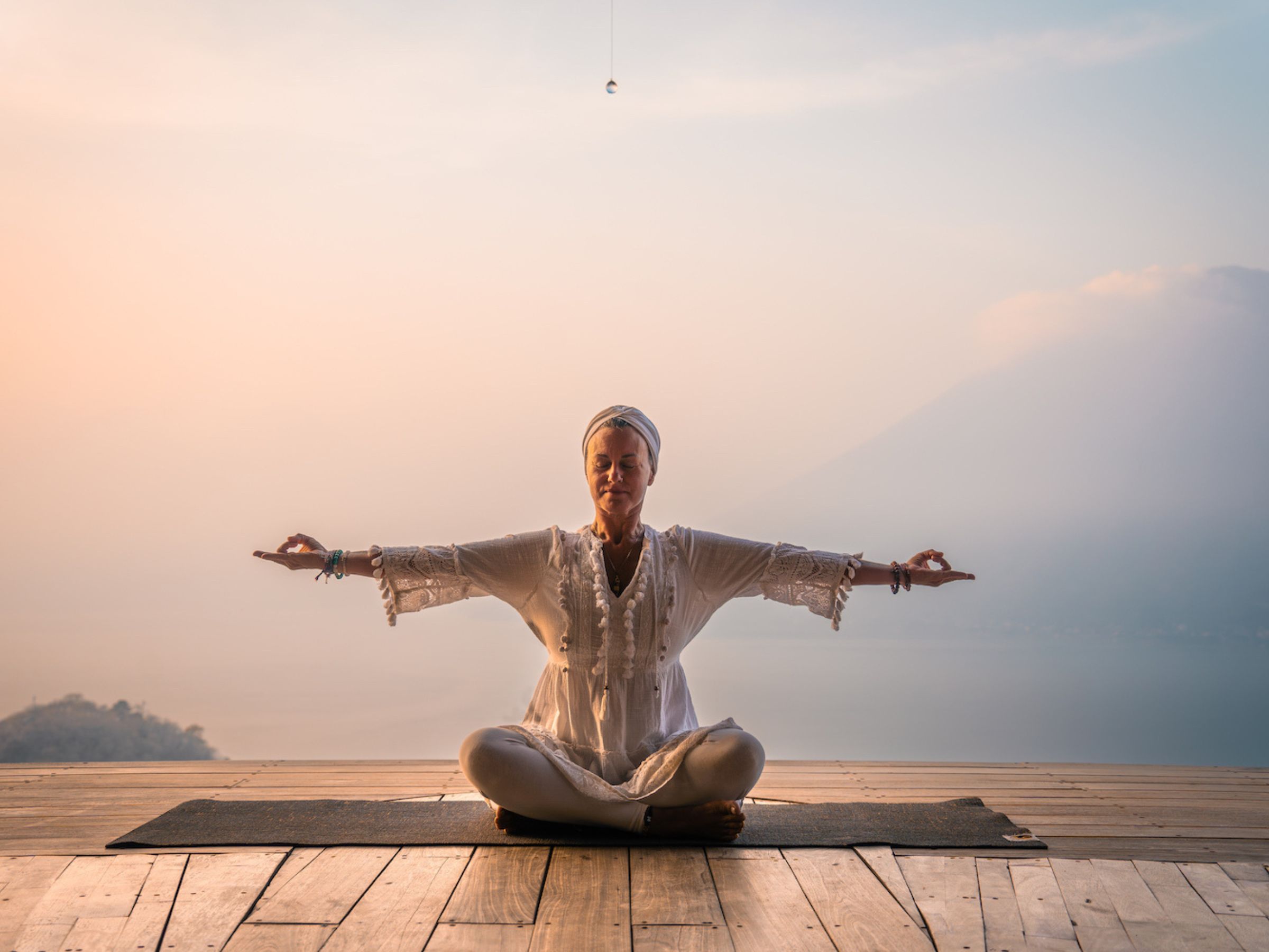 Photograph of Geet Fateh Kaur dressed in white practising kundalini yoga dressed in white with sunset behind her.